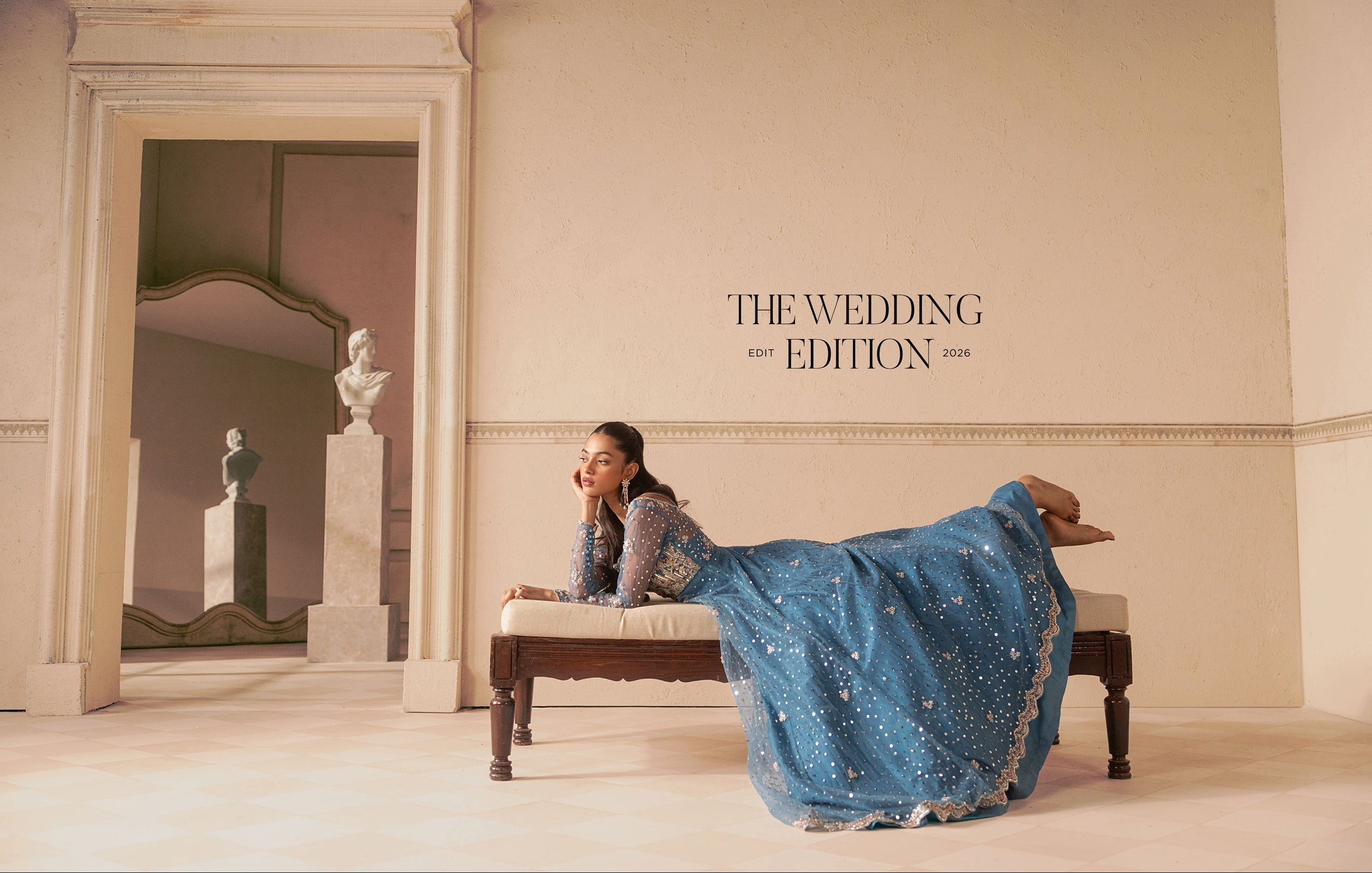 A woman in a sparkling blue traditional gown reclines on a bench in a classical interior setting. The text 'THE WEDDING EDITION' is printed on the wall behind her.
